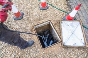 A man is unblocking a drain by putting a hose into a hole in the ground.