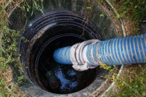 A plumbing professional lowering a pipe into a manhole.